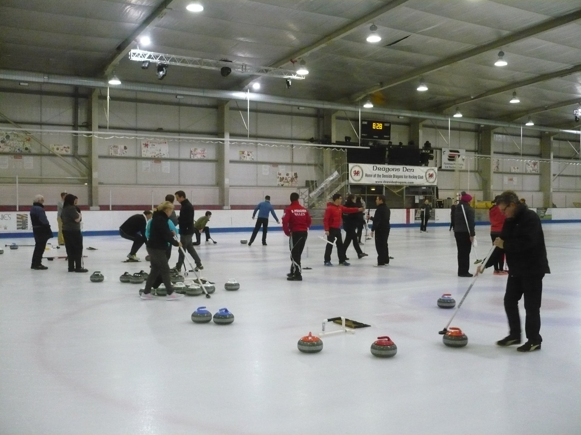 Photograph of one end of the ice rink, with players talking and getting ready to play shots
