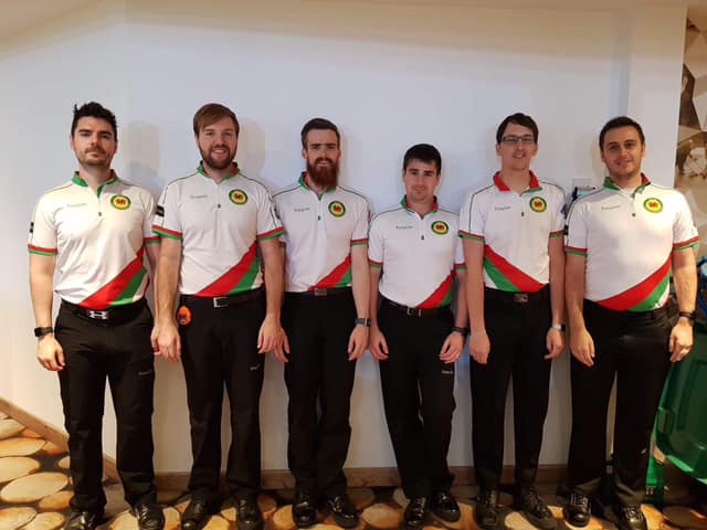 Photograph of 6 white men, all brunette, stood in a row wearing black trousers and white tops with red and green stripes on them