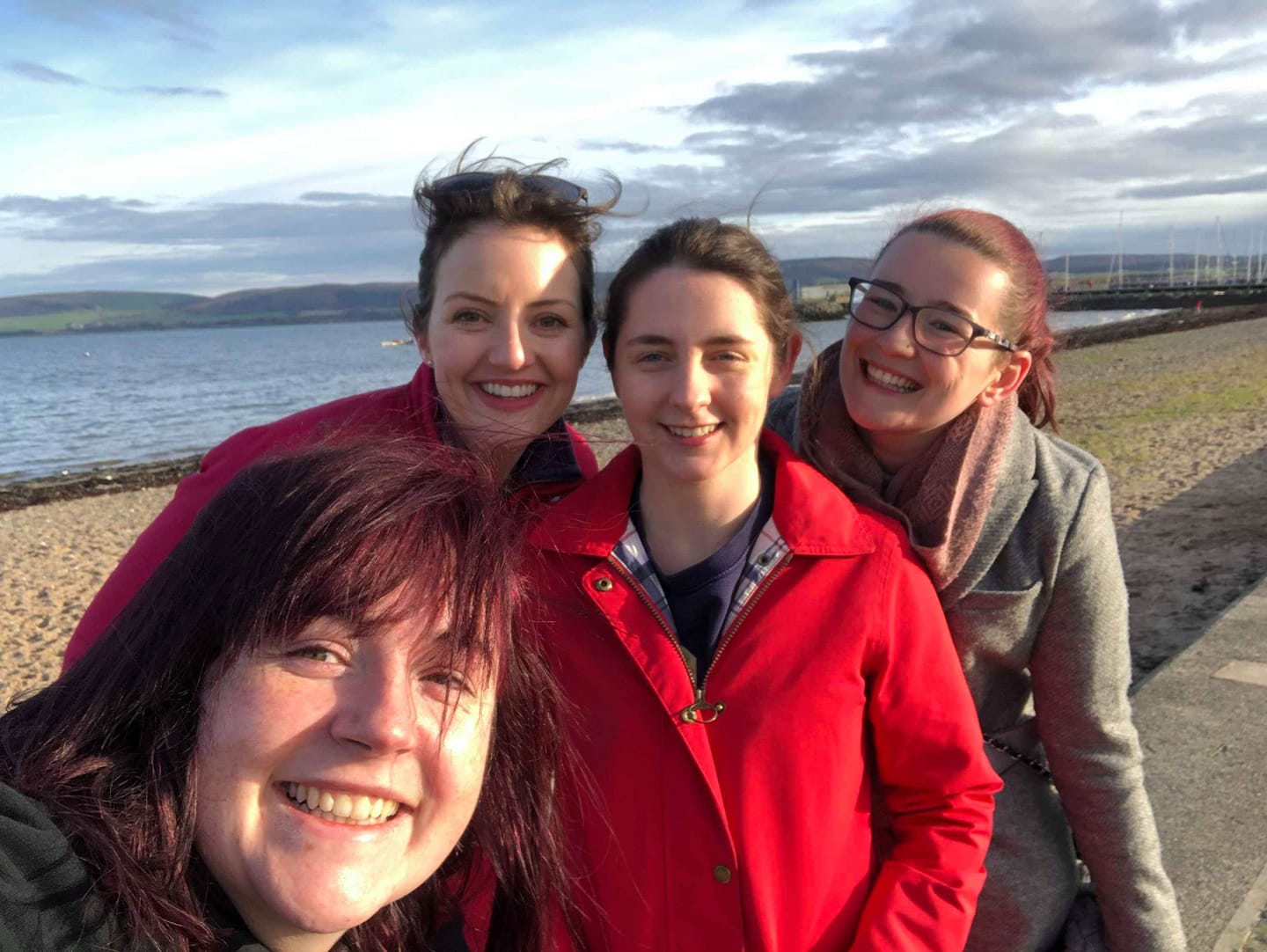 Photograph of four white women in their twenties and thirties, stood on a beach.