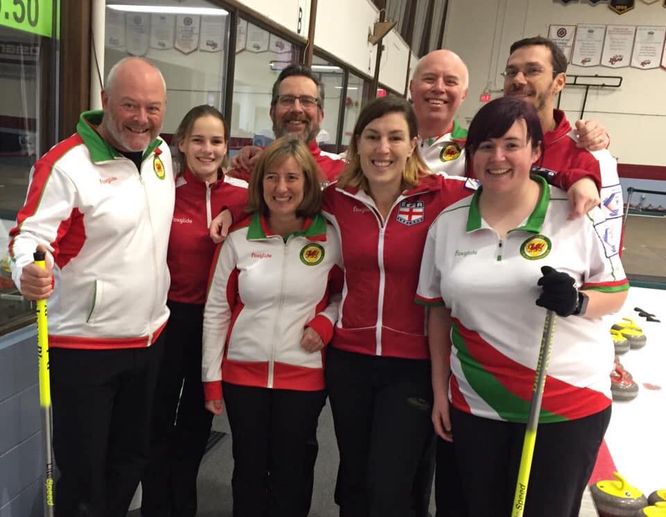 Photograph of the Welsh team, wearing white, and the English team, wearing red. There are four women and four men.